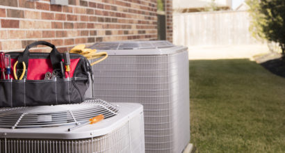 Bag of repairman's work tools, screwdriver on top of an air conditioner unit outside a residential home's back yar